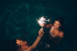 Cheerful friends burning sparkles near pool