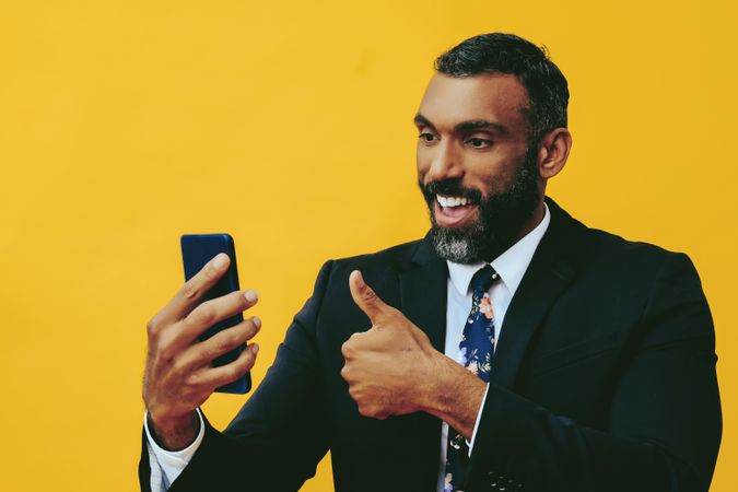 Smiling Black businessman in suit giving thumbs up at smartphone screen