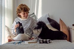 Glad schoolboy with retro photo camera and dog on bed