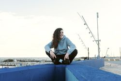 Young teenage girl sitting on a stone wall with her legs crossed while smiling