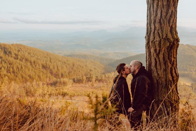 Smiling men hugging near tree in forest on hill