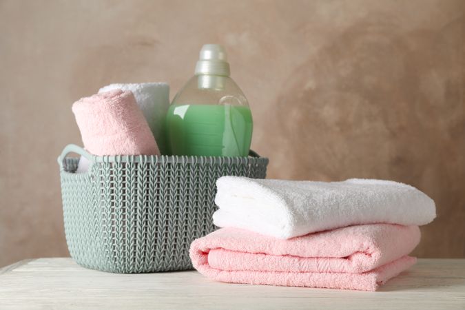 Basket with clean towels and laundry liquid on wooden background, space for text