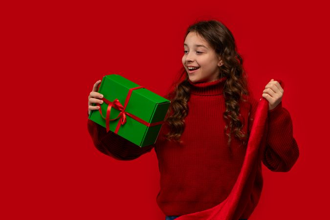 Excited girl holds Christmas gift and Santa hat.