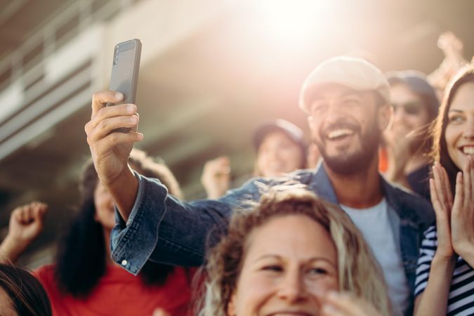 Young man and woman taking selfie at stadium with spectators around