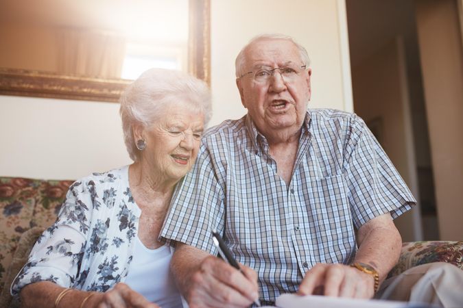 Mature man and woman sitting on sofa and signing some paperwork
