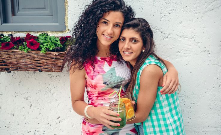 Two female friends holding each other with fruity cocktails 