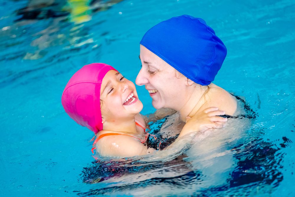 Cheerful girl swimming in pool with mother