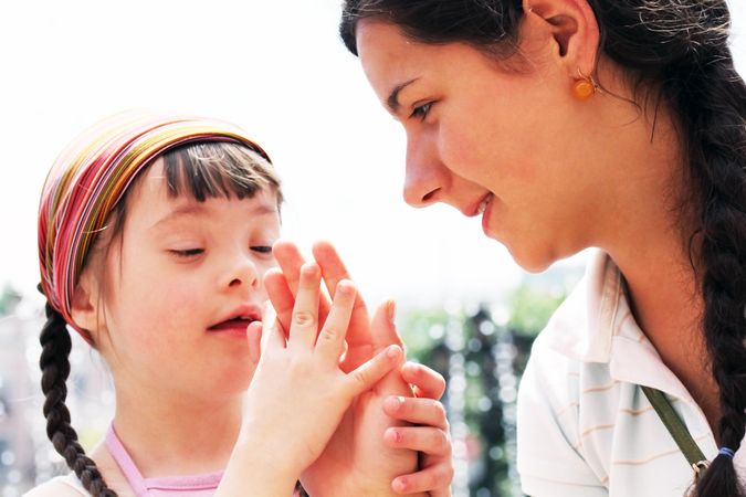A teenager and young girl with Down syndrome putting their hands together outside