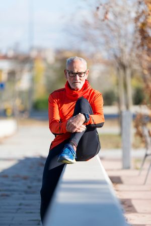 Older male holding knee while sitting on divide in park