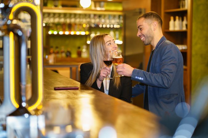 Man and woman smiling while toasting beer and wine at a bar or lounge