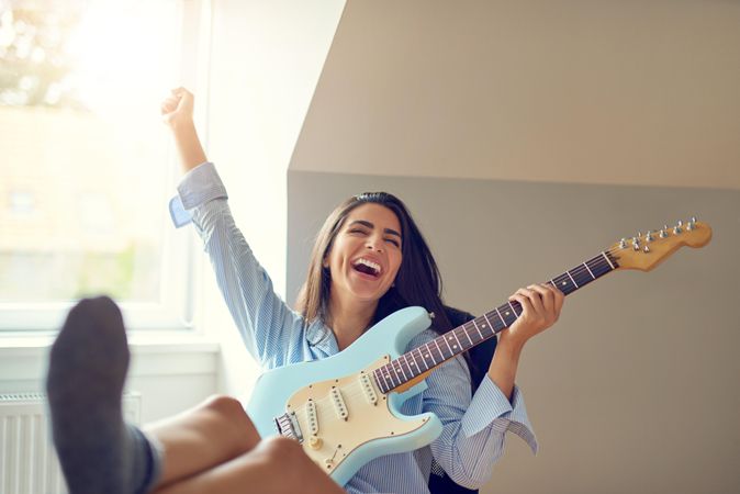 Woman having fun and laughing while playing guitar at her desk