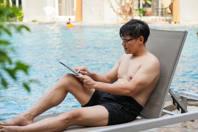 Man reading on digital reader by poolside