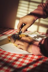 Pizza with basil being cut with knife and fork on a plate at table