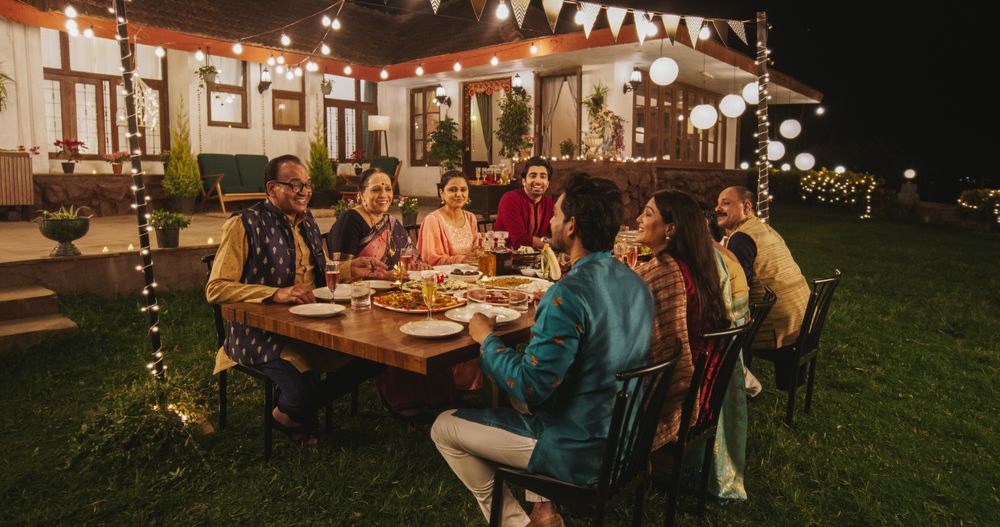 Big Indian Family Celebrating Diwali: Family Gathered Together on a Dinner Table in a Backyard Garden Full of Lights.