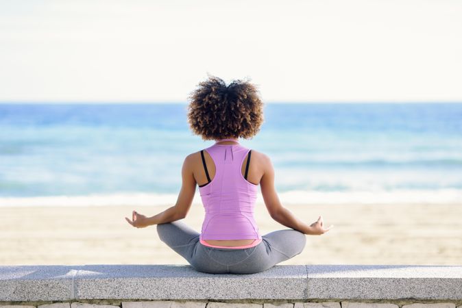 Rear view of Black woman with afro hairstyle meditating on the beach