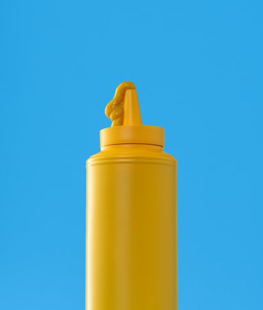 Mustard plastic bottle close up, minimalist on a blue background