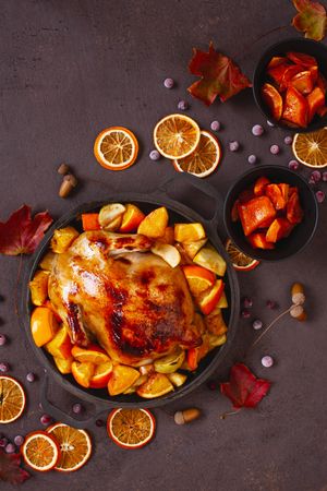 Seasonal table with roasted chicken pot, oranges, autumn leaves and berries