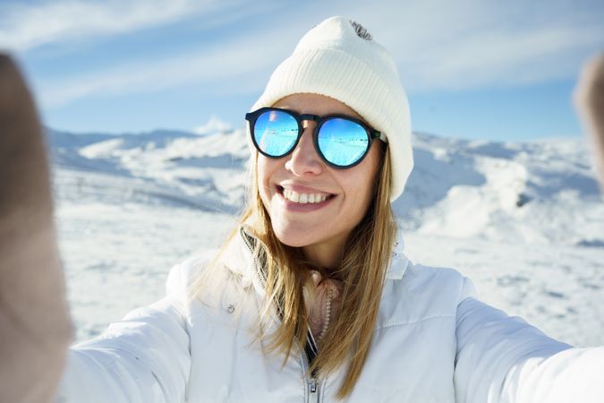 Female in warm clothes beanie cap, and polarized sunglasses smiling while taking selfie
