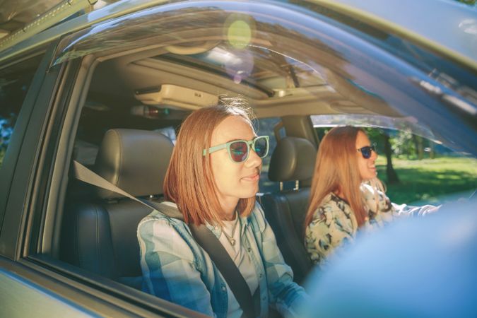 Two happy young women in sunglasses traveling in car