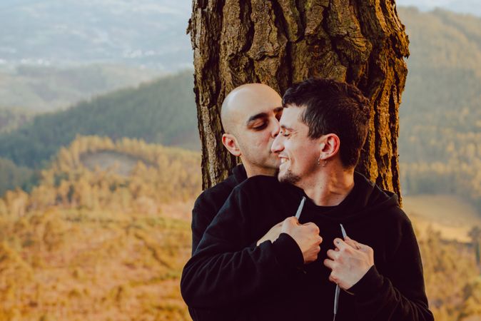 Smiling men hugging near tree in forest on hill