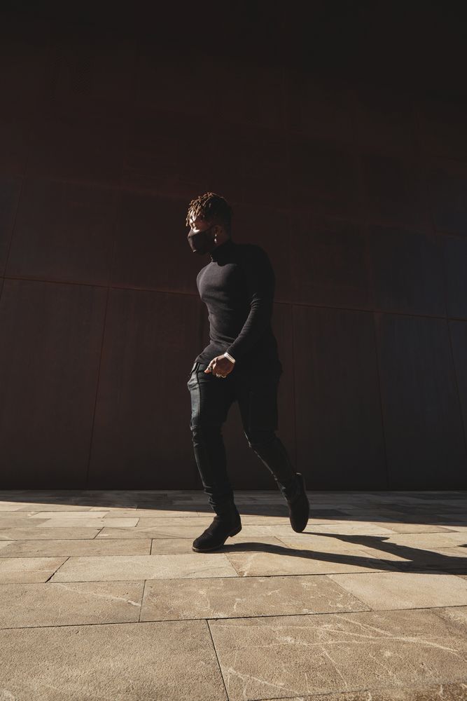Stylish Black man walking on pavement in dark clothes