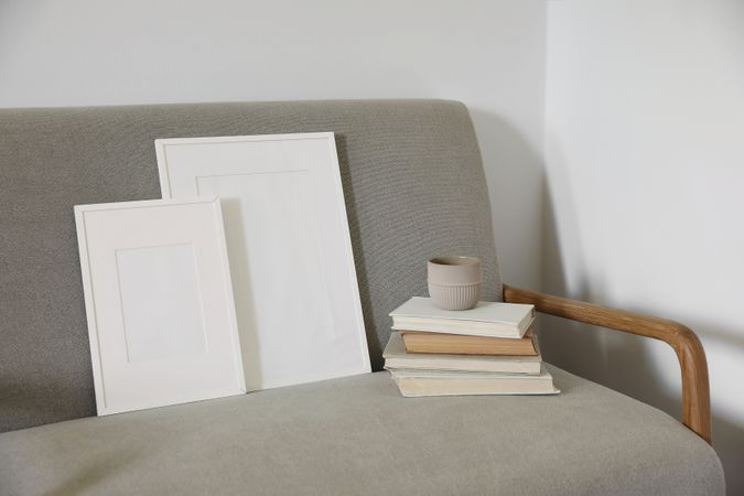 Elegant still life of two blank frames, a pile of books and coffee on sofa