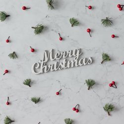 Holly and pine pattern on marble background with the words “Merry Christmas”