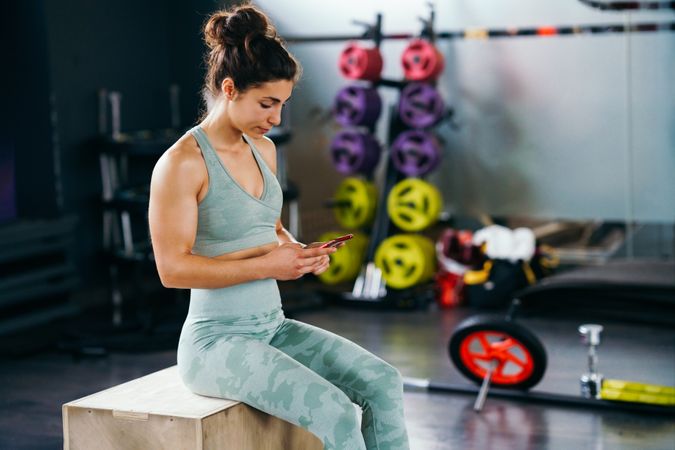 Woman texting on her phone in between gym workouts