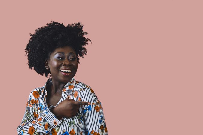 Studio shot of smiling Black woman in floral print shirt pointing her finger to the side