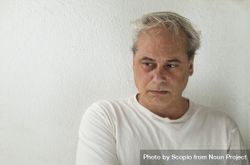 Portrait of middle aged man in light shirt looking away and thinking against light wall bekPp5