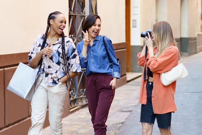 Three laughing women walking down narrow lane and taking photos
