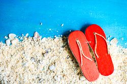 Flat lay of flip flips and sand on blue background