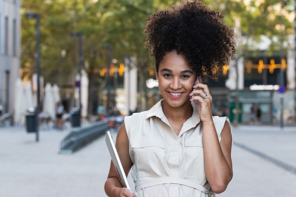 Smiling Black pregnant woman talking on smartphone and carrying a laptop