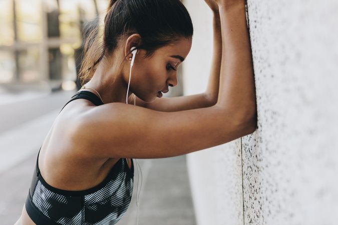 Fitness woman standing outdoors with forearms to the wall