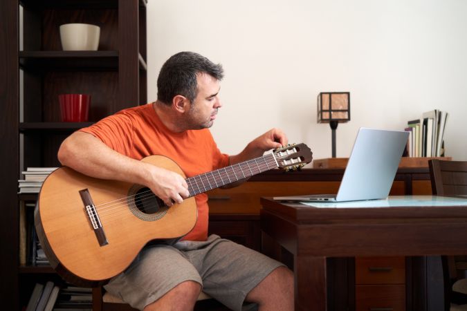 a man with a laptop computer in online guitar lessons learning how to tune his guitar