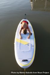 Woman in child’s pose on paddleboard on the water 481RXb