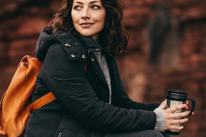 Beautiful woman wearing jacket sitting outdoors and looking away