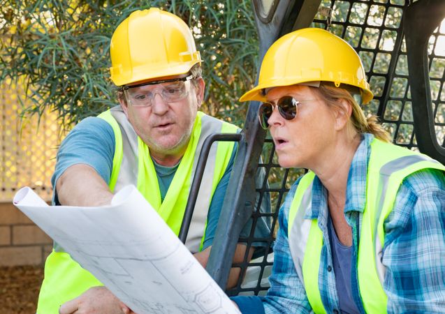 Male and Female Workers With Technical Blueprints Talking at Construction Site