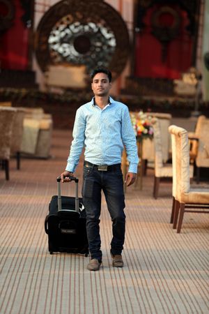 Young man in blue dress shirt walking with luggage