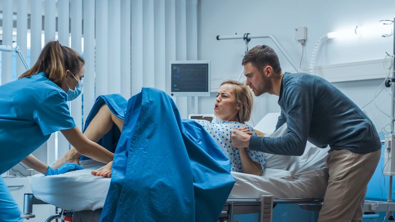 In the Hospital, Woman in Labor Pushes to Give Birth, Obstetricians and Doctors Assist, Her Husband Supports Her by Holding Hand
