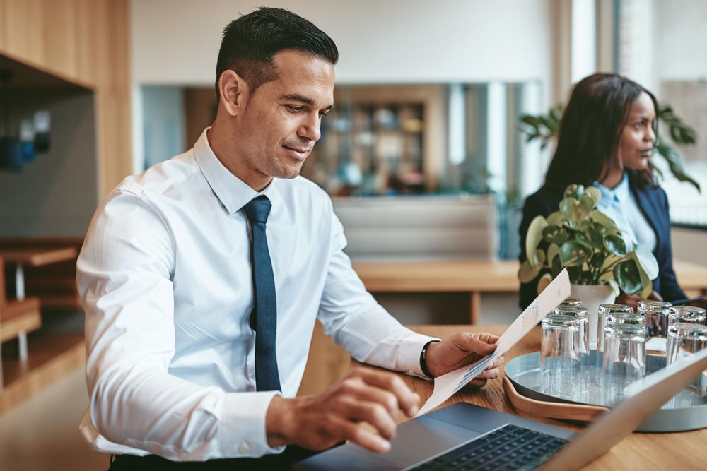 Man holding paper and typing at a laptop in a bright open office