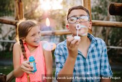 Boy blowing soap bubbles while an excited girl enjoys the bubbles 4mk8X0