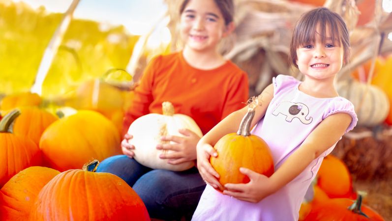 Two Girls Holding Their Pumpkins At A Pumpkin Patch on a Fall Day.