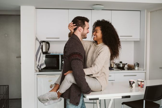 Cheerful multiracial couple hugging in kitchen