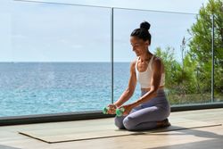 Slim sportswoman training with dumbbells on terrace against sea