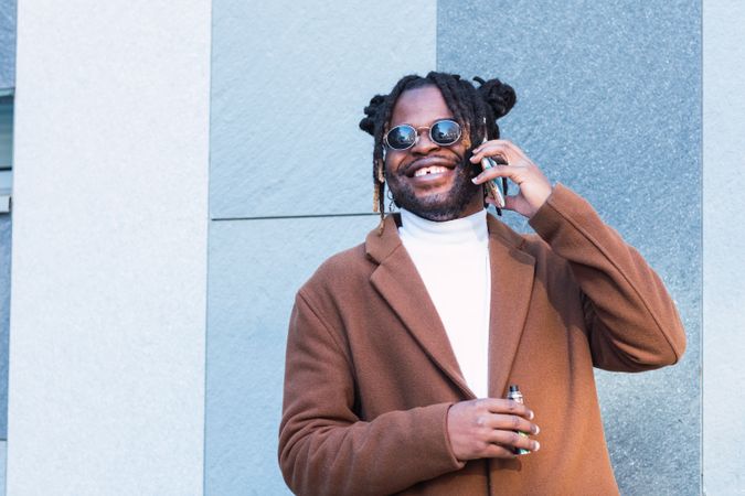 Cheerful Black man with electronic cigarette talking on smartphone