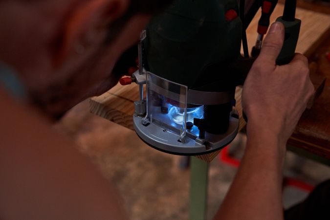 Crop male carpenter grinding wooden plank using special equipmen