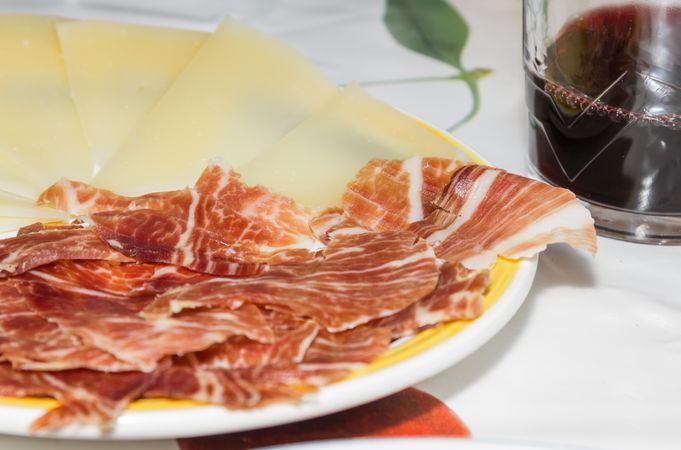 Typical spanish tapa with slices of serrano ham and manchego cheese, accompanied with a glass of Rioja red wine