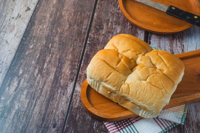 A loaf of bread served on a wooden plate placed on a rustic wooden surface