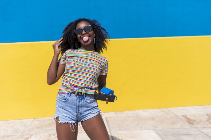 Black woman with tongue out in front of bright yellow and blue wall